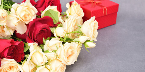Side view of a lying bouquet of red and white roses. There is a slightly blurred gift box in the background.