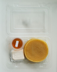 Stack of pancakes in a container transparent clear box with honey and butter isolated on white background.