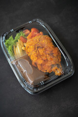 Chicken Chop and fries with  Black Pepper sauce and vegetables. in a take away container.