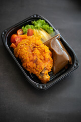 Chicken Chop and fries with  Black Pepper sauce and vegetables. in a take away container.