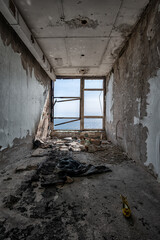 Sea view through the window of a room in an abandoned building with various trash and debris on the floor and a woman's shoe in the foreground
