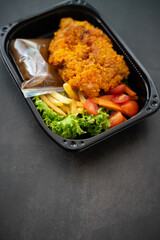 Chicken Chop and fries with  Black Pepper sauce and vegetables. in a take away container.