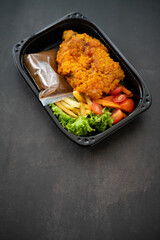 Chicken Chop and fries with  Black Pepper sauce and vegetables. in a take away container.