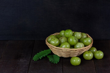 Pile of Indian gooseberry fruits or Amla (phyllanthus emblica) on wicker basket on wooden background, dark tone.