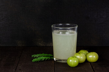Indian gooseberry fruit and juice or Amla (phyllanthus emblica) on wooden background, dark tone.