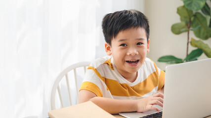 happy cute little school boy doing homework and using laptop at home