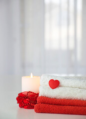 Obraz na płótnie Canvas Red and white towels with heart and candle with red decor. Spa, massage salon, relax and wellness. Valentine's Day atmosphere: heart, love, care, romance, health. Copy space.
