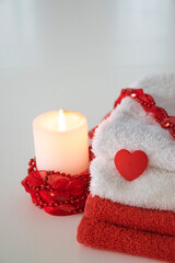 Red and white towels with heart and candle with red decor. Spa, massage salon, romantic relaxation concept. Laundry, washing or dry cleaning concept. Copy space.