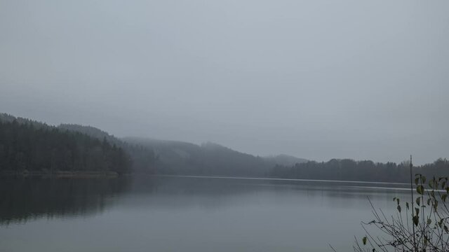 Nebelschwaden &uuml;ber einem Stausee mit h&uuml;geligem, bewaldetem Ufer als Zeitraffer