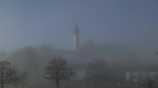Kloster Andechs mit dem Kirchturm hinter Nebelschwaden vor blauem Himmel als Zeitraffer