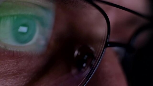 Close up view on male eye in glasses looking at pc monitor at night. Internet surfing and addiction.