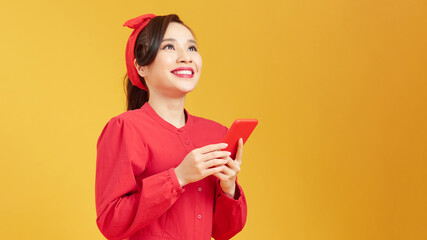 Cheerful asian woman using smartphone and rejoice over yellow background