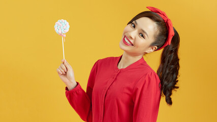 Sweet and extremely big. Beautiful young woman holding a big lollipop while standing against yellow background