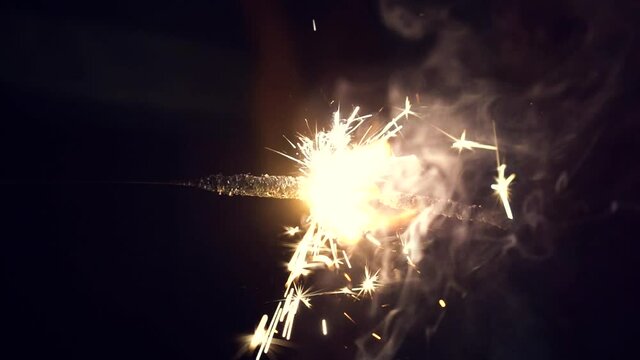 slow motion shot of lit Phuljhadi with sparks flying out against a dark black background with blue smoke coming out shot on the indian festival of Diwali
