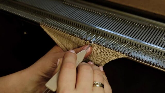 Knitting on a knitting machine, working on a machine. Needlework, hands close-up.