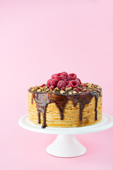 Pancake cake with caramel drops, walnuts and raspberries on a pink background. Maslenitsa or Shrovetide.