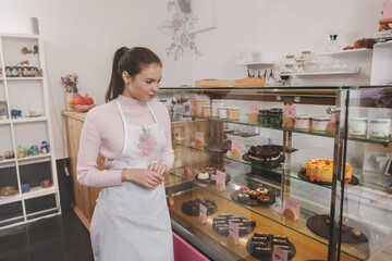 Fototapeta na wymiar Beautiful young woman wearing apron, working at her vegan desserts cafe