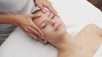 Young, beautiful and healthy woman in massaging salon. Traditional face massage therapy and skin care.