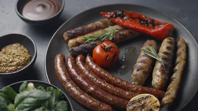The girl pricks a grilled sausage on a fork. A plate with sausages, lettuce, vegetables. The camera is moving