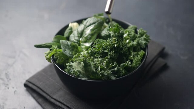 A girl pours olive oil over a salad of fresh green lettuce leaves. Dark background, the camera moves on the salad
