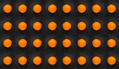 A pattern of oranges on a black stone background, texture, top view, close up.