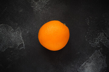 An orange on a Black stone background, texture, top view, close up.