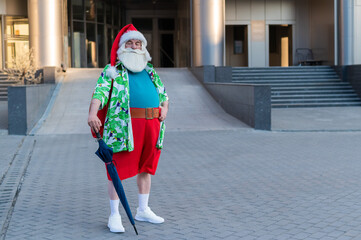 Santa Claus dressed in shorts walks around the city with an umbrella