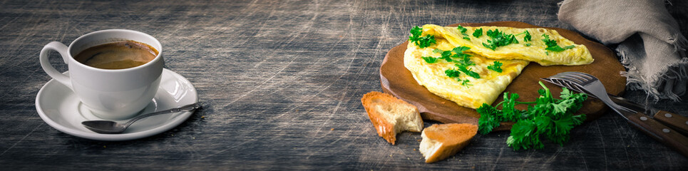 Banner a traditional French omelet with toasts and butter, chopped parsley and a white porcelain cup of coffee on a wooden board placed on a dark wooden table and dark wooden background, copy space