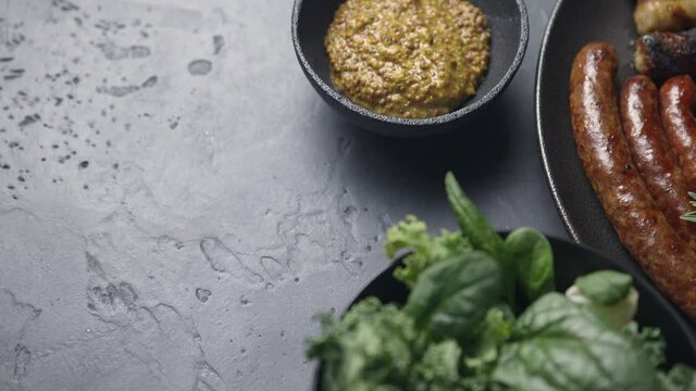 A dish of grilled sausages, tomatoes, lemon, vegetables. Fresh salad, dark background, mustard, place for text. The camera moves to the side