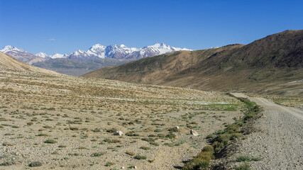 Scenic landscape view with dirt road and snow-capped mountains at high-altitude Khargush pass, Gorno-Badakshan, Tajikistan Pamir