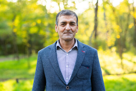 Headshot Of Happy Old Mature Asian Man With Black Gray Hair Wearing Jacket And Shirt Smiling Positive And Looking At Camera In Park. Senior Asian Male Portrait With Retirement Concept.