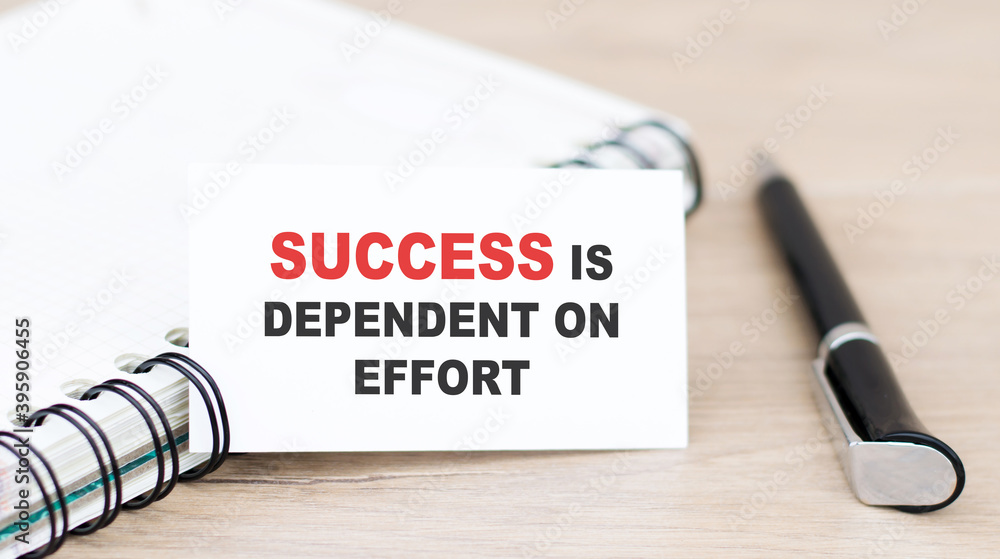 Poster text success is dependent on effort on a white card, which is next to the notebook and pen on the ta