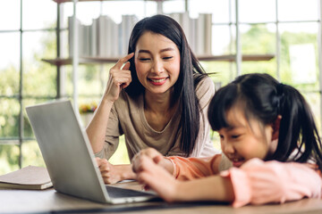 Mother and asian kid little girl learning and looking at laptop computer making homework studying knowledge with online education e-learning system.children video conference with teacher tutor at home