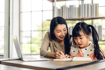 Mother and asian kid little girl learning and looking at laptop computer making homework studying knowledge with online education e-learning system.children video conference with teacher tutor at home