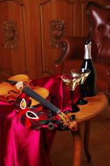 Two glasses of wine, a bottle, a violin, a carnival mask on a table with burgundy drapery.