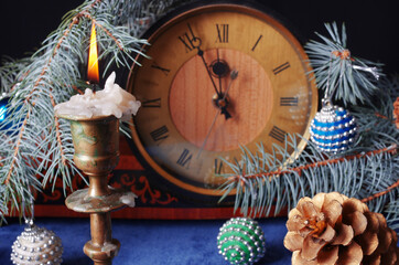 Burning candle, clock face, fir branch and Christmas decorations.