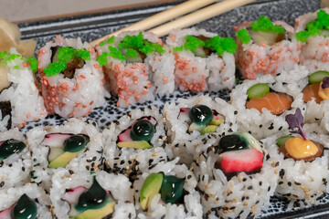 close up of an assortment of delicious uramaki with out of focus pickled ginger and chopsticks