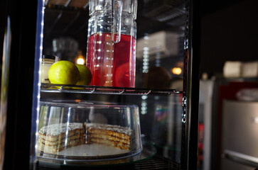 Blurry image of Showcase in cafe shop. Cake and jug with drink on the shelves of a window of a street restaurant
