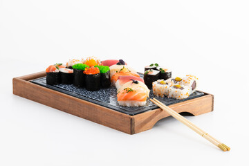 view of assorted maki, nigiri and uramaki with chopsticks on a wooden tray on a light background.