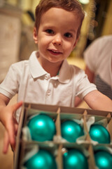 Obraz premium A little boy with ornaments for a Christmas tree posing for a photo at home. Together, New Year, family, celebration