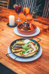 Gourmet dinner at the table, Spanish Paella and grilled meat, fresh and colorful drinks. Rustic and cozy setting.