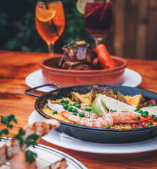 Gourmet dinner at the table, Spanish Paella and grilled meat, fresh and colorful drinks. Rustic and cozy setting.