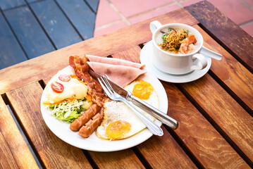 The English breakfast consists of fried eggs, bacon, sausage, and green salad, And Thai rice soup with shrimps With a beach backdrop at Thailand