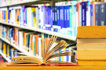 A pile of books and open book with blurred library bookshelf as background and copy space