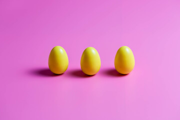 Three Yellow Plastic Easter Eggs on pink background