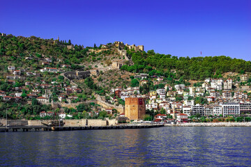 Fototapeta na wymiar View from the sea to the Old City of Alanya (Turkey). Kizil Kule, Alanya Kalesi, ancient wall and modern cottages on the Mediterranean coast