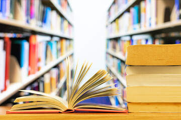 A pile of books and open book with blurred library bookshelf as background and copy space
