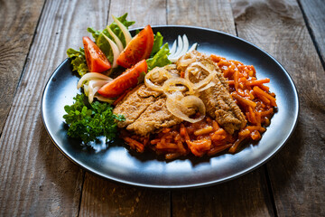 Fish dish - fried fish fillet on vegetable sauce on wooden table

