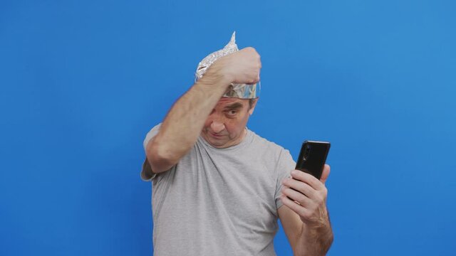 Frightened man in a tinfoil hat waved off the 5G waves.5G tower radiation protection. Irrational fear of a non-existent problem. Protective foil helmet to the brain from aliens.