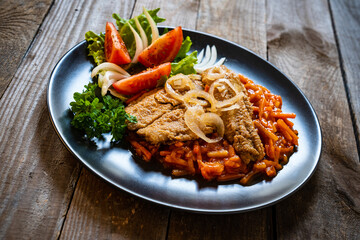Fish dish - fried fish fillet on vegetable sauce on wooden table
